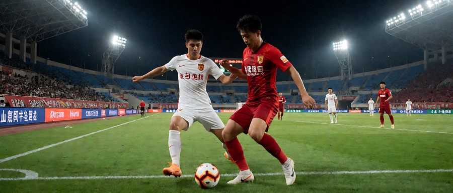 夜间足球比赛现场，灯光照亮整个球场，双方球员在中场区域激烈拼抢，场边广告牌清晰可见